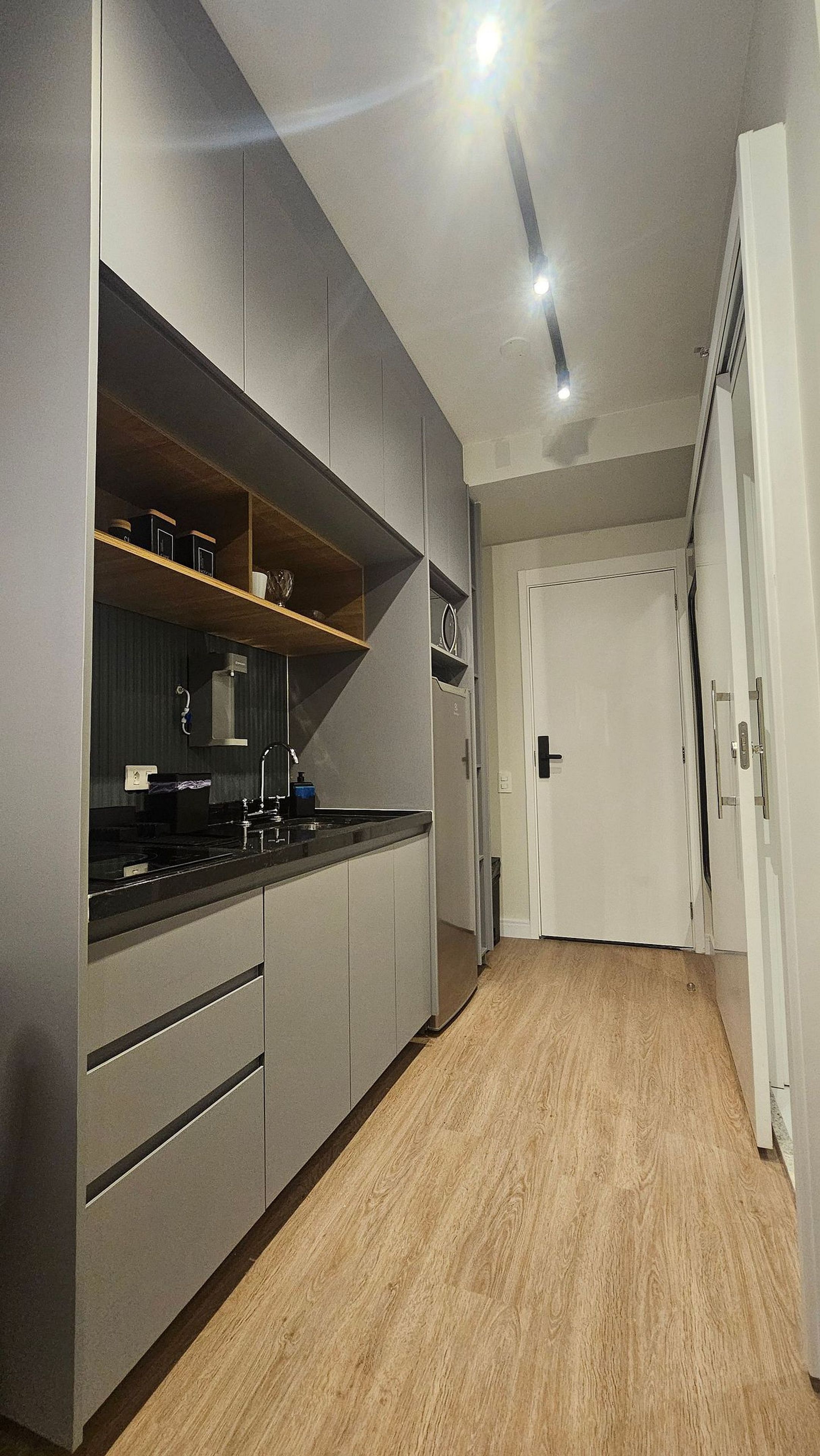 Une cuisine moderne avec des meubles de couleur grise, un plan de travail noir et un plancher en bois.