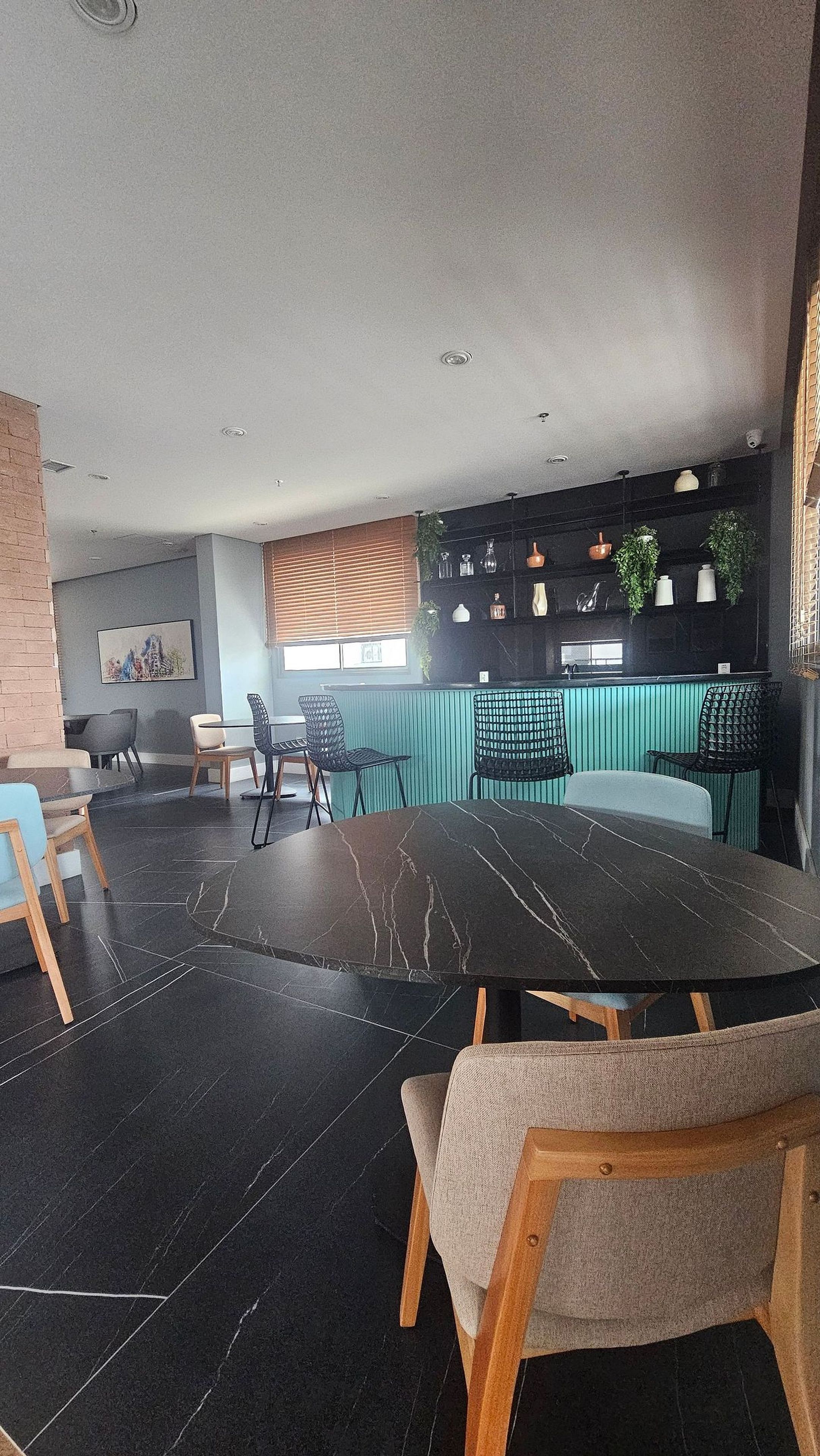 Un interno moderno con zona pranzo che include un tavolo e sedie in marmo nero, angolo cottura con piano di lavoro nero e diversi utensili da cucina, e mensola a parete con oggetti decorativi.