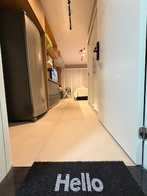 A hallway leading to a bedroom with a bed, a door, and a refrigerator. - Condominio Hub Brooklin (São Paulo)