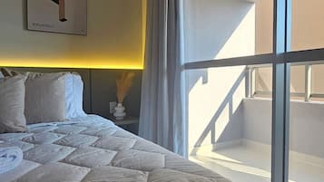 A hotel room with a large bed, a nightstand, a framed picture on the wall, and a view of the outside balcony.