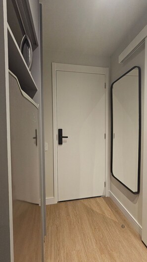 A room with a white door, a mirror on the wall, and a wooden floor. - Condominio Hub Brooklin (São Paulo)
