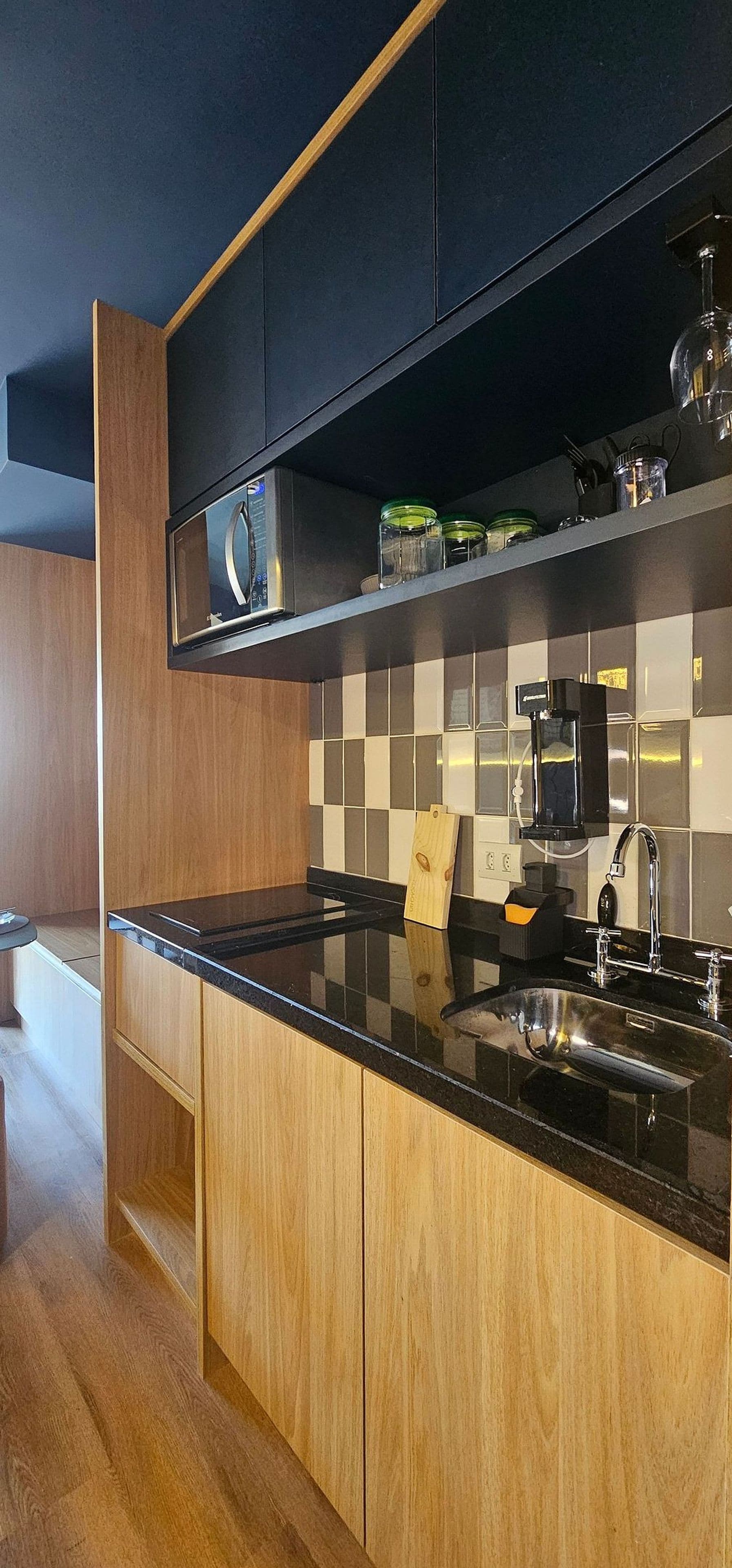 Cozinha moderna com bancada preta, armários de madeira, pia de aço inoxidável e painel de parede preto.