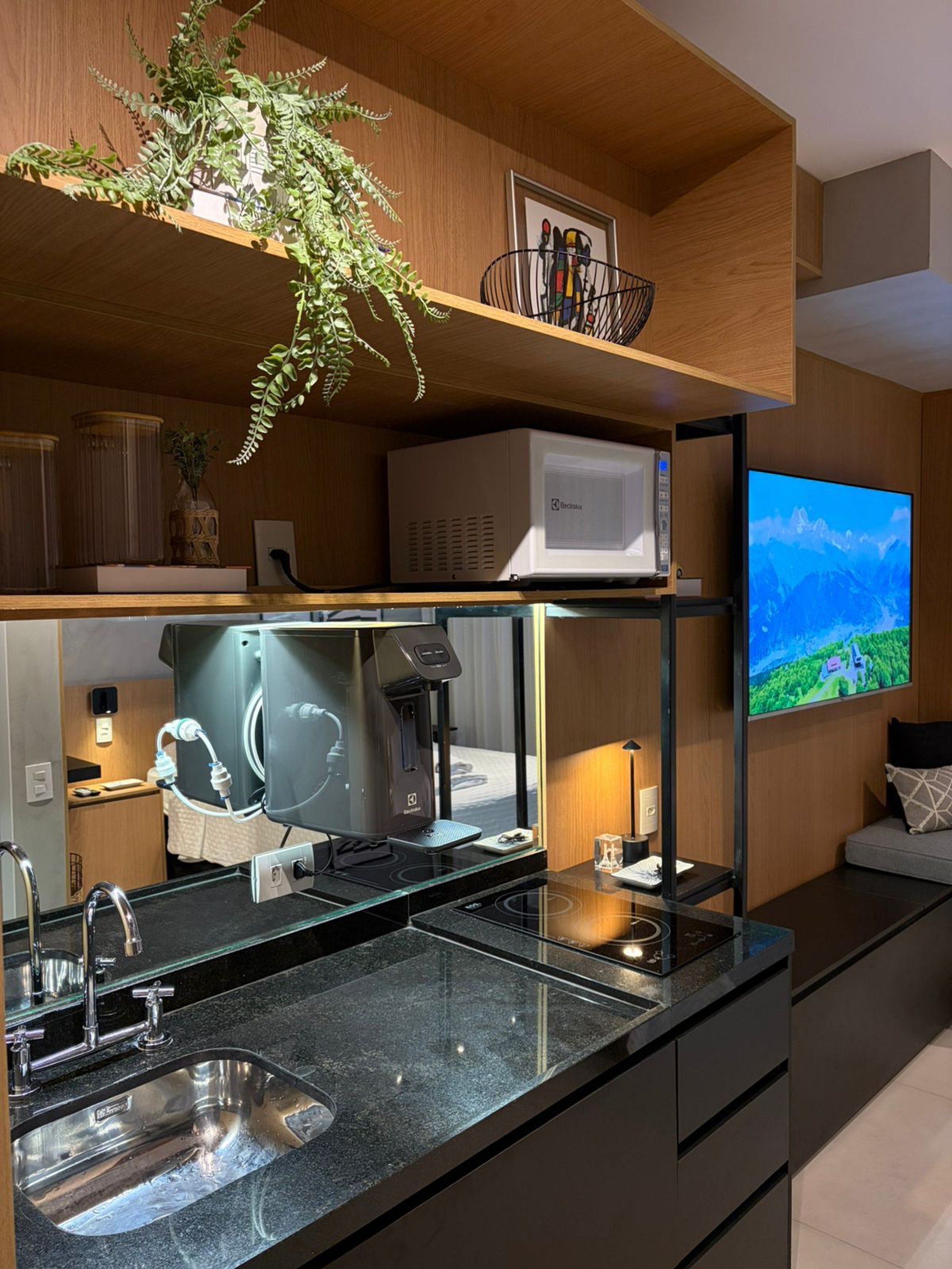 A modern kitchen with a built-in microwave, a coffee machine, and a large flat-screen TV mounted on the wall.