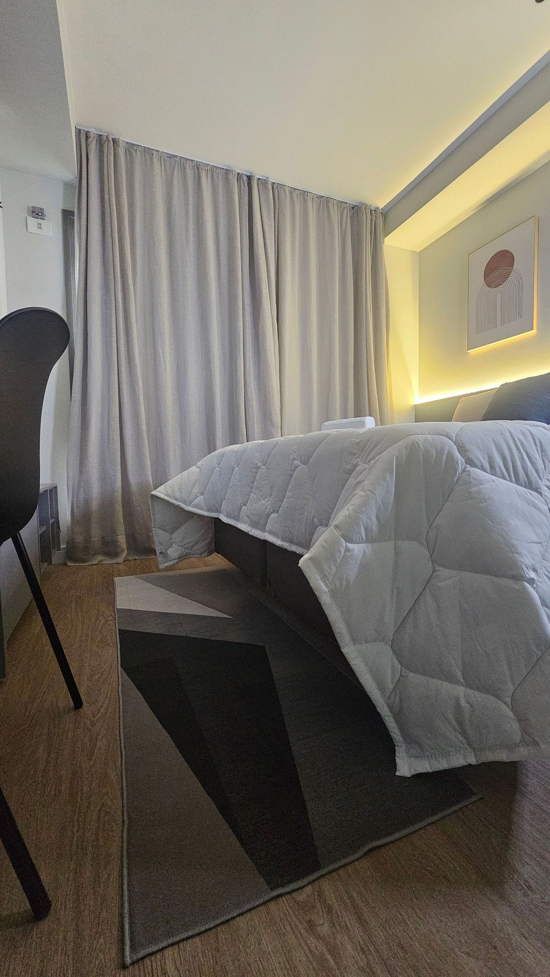 A hotel room with a bed, a chair, a rug, and a wall-mounted light fixture.