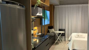 Um quarto de hotel moderno com cozinha compacta, TV de tela plana, cama com edredom branco e área de jantar com mesa e cadeiras.