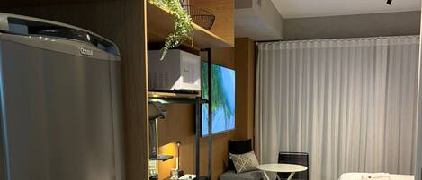 Um quarto de hotel moderno com cozinha compacta, TV de tela plana, cama com edredom branco e área de jantar com mesa e cadeiras.