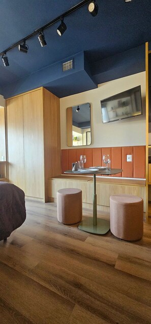 A modern interior with a wooden floor, a bar area with stools, and a television mounted on the wall. - Condominio Hub Brooklin (São Paulo)