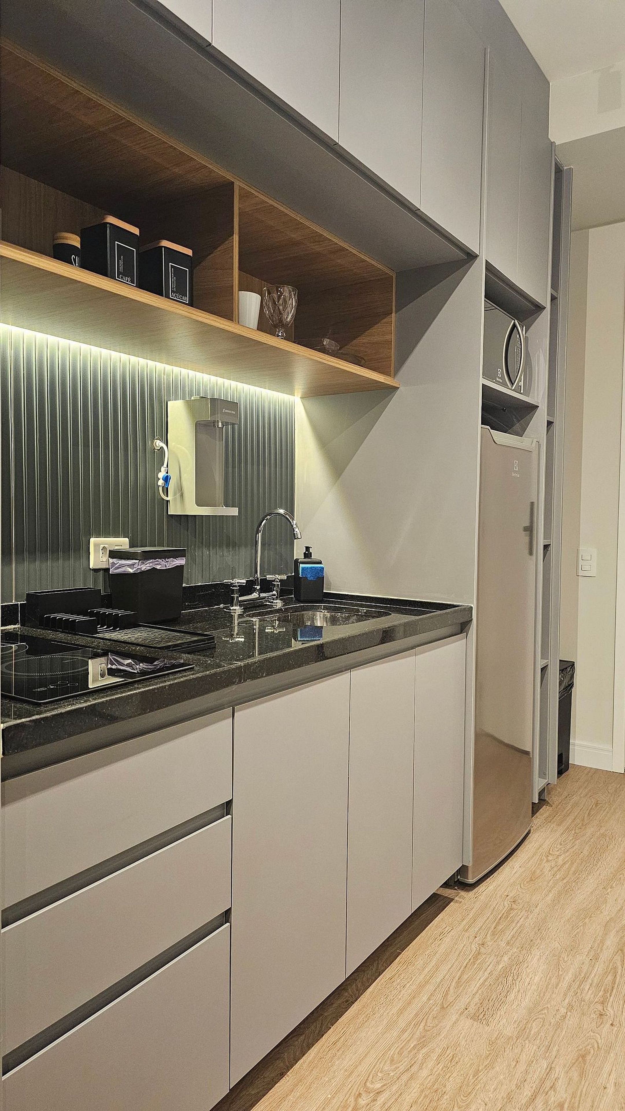 A modern kitchen with a built-in stove, a sink, and a wooden shelf above the countertop.