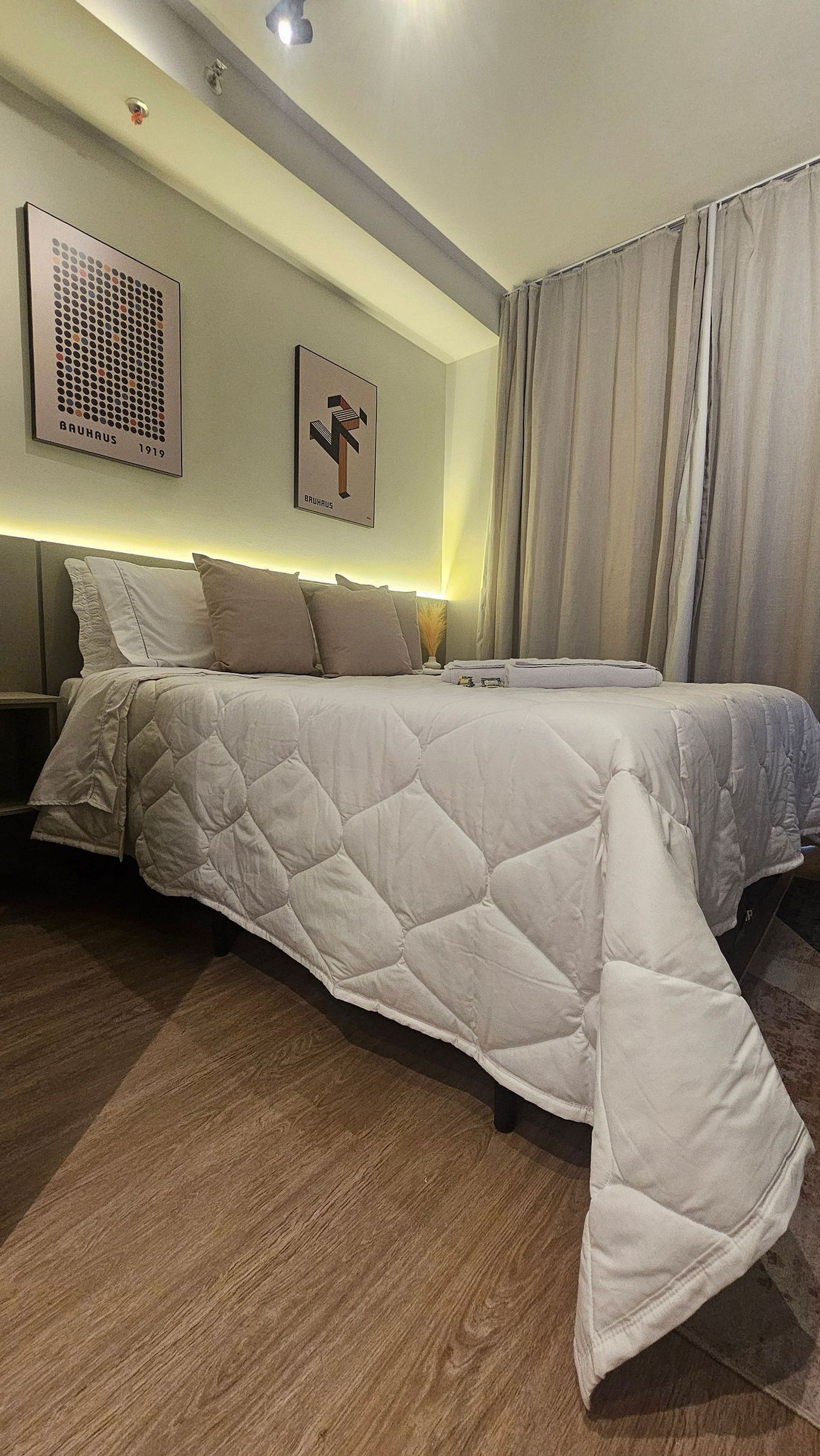 A modern bedroom with a large bed, a headboard, a wall-mounted artwork, and a window with curtains.