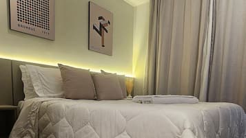 A modern bedroom with a large bed, a headboard, a wall-mounted artwork, and a window with curtains.