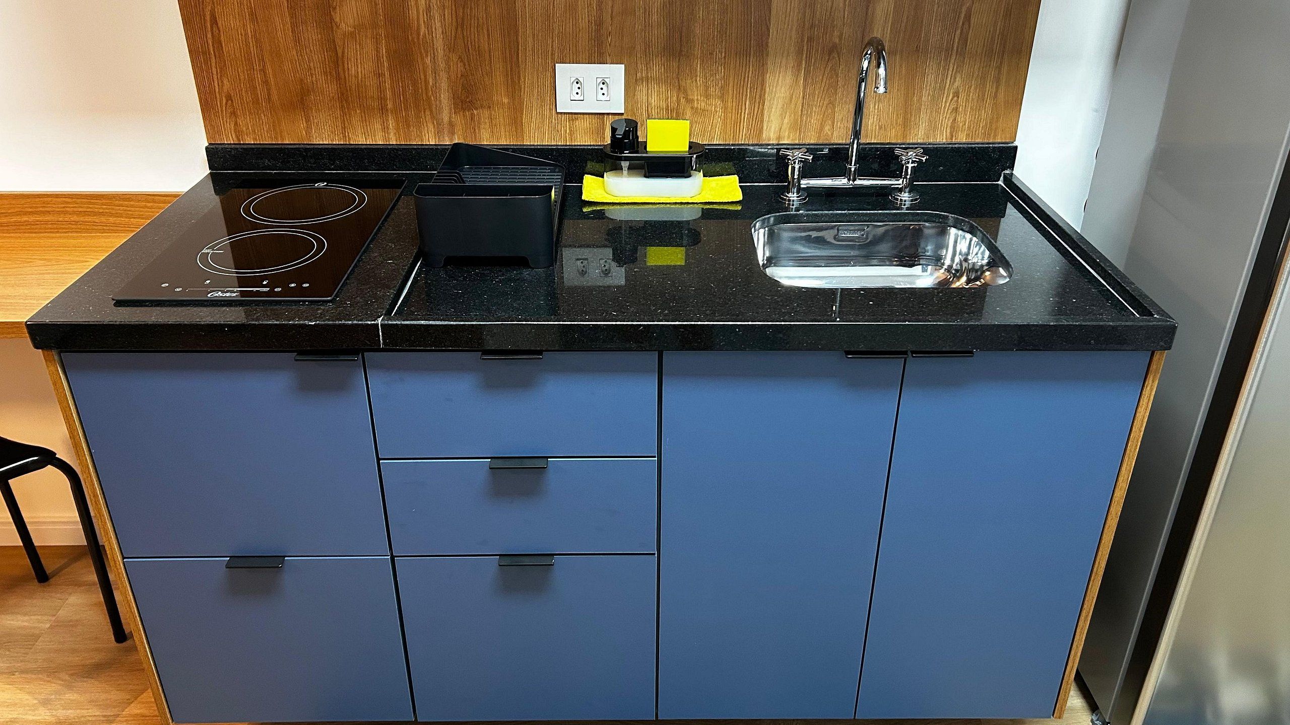 A kitchen with a black countertop, a built-in stove, a sink, and blue cabinets.