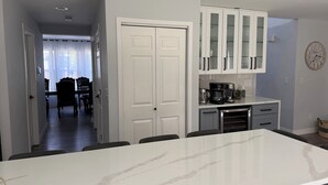 Una cocina moderna con armarios blancos, encimera de mármol y un comedor con mesa y sillas.