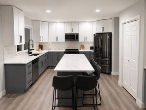 A modern kitchen with white cabinets, a central island with bar stools, stainless steel appliances, and a wooden floor.
