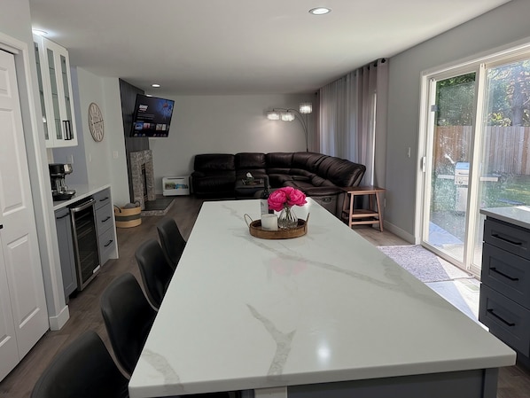 Una cucina moderna con isola centrale, un'area pranzo con tavolo bianco e un soggiorno con divano in pelle scura.