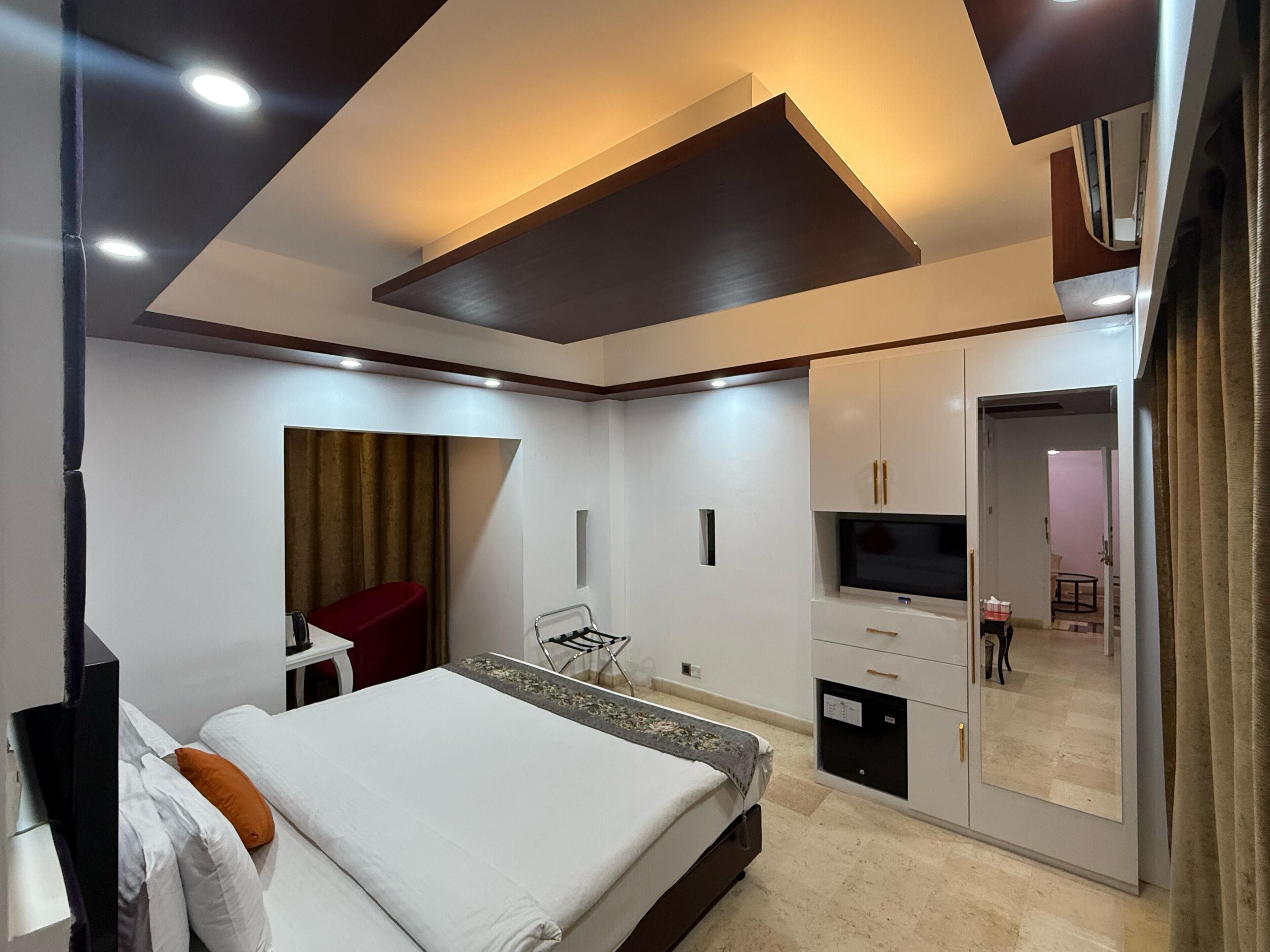 A modern hotel room with a bed, a TV, a wardrobe, and a desk.