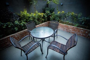A round glass table with four wicker chairs in an outdoor patio area. - Elite Hotel Airport (Dhaka)