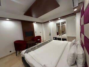 Una habitación de hotel con cama, escritorio, dos sillas, televisor y espejo.