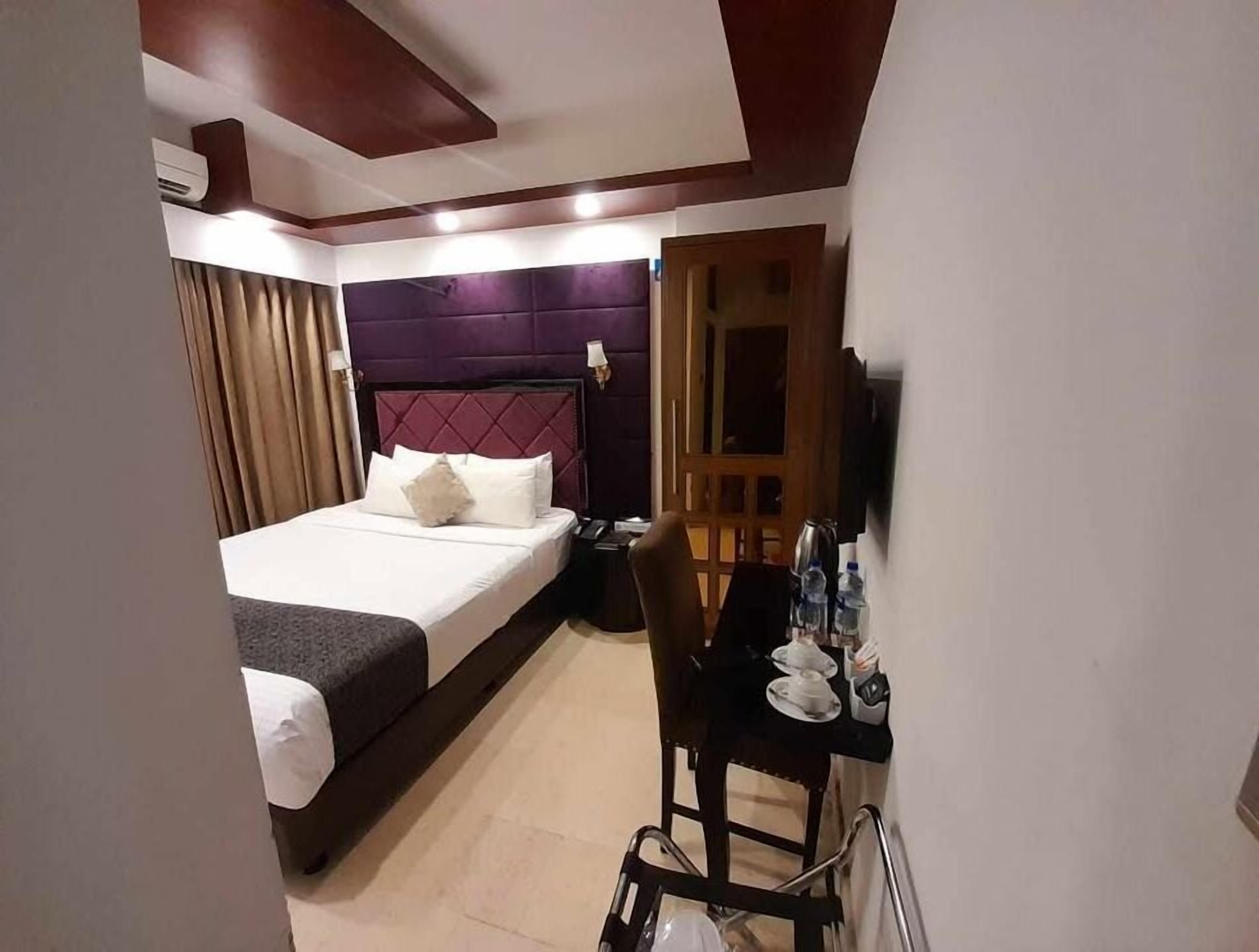 A hotel room with a bed, a desk, a chair, a wardrobe, and a television.