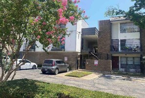 A residential building with a two-story structure, a parking area with cars, and a tree with pink flowers. - Warm & Cozy Condo Feels Like Home (Dallas)