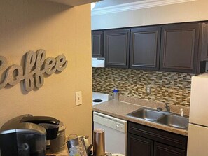 Eine Küche mit dunklen Schränken, einer gefliesten Spritzschutzwand und einem Schild mit der Aufschrift 'Kaffee'.