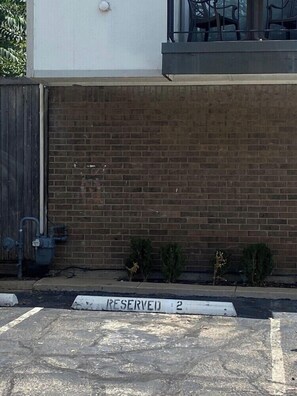 Um muro de tijolos com uma cerca de metal, uma pequena planta e o sinal de vaga reservada.