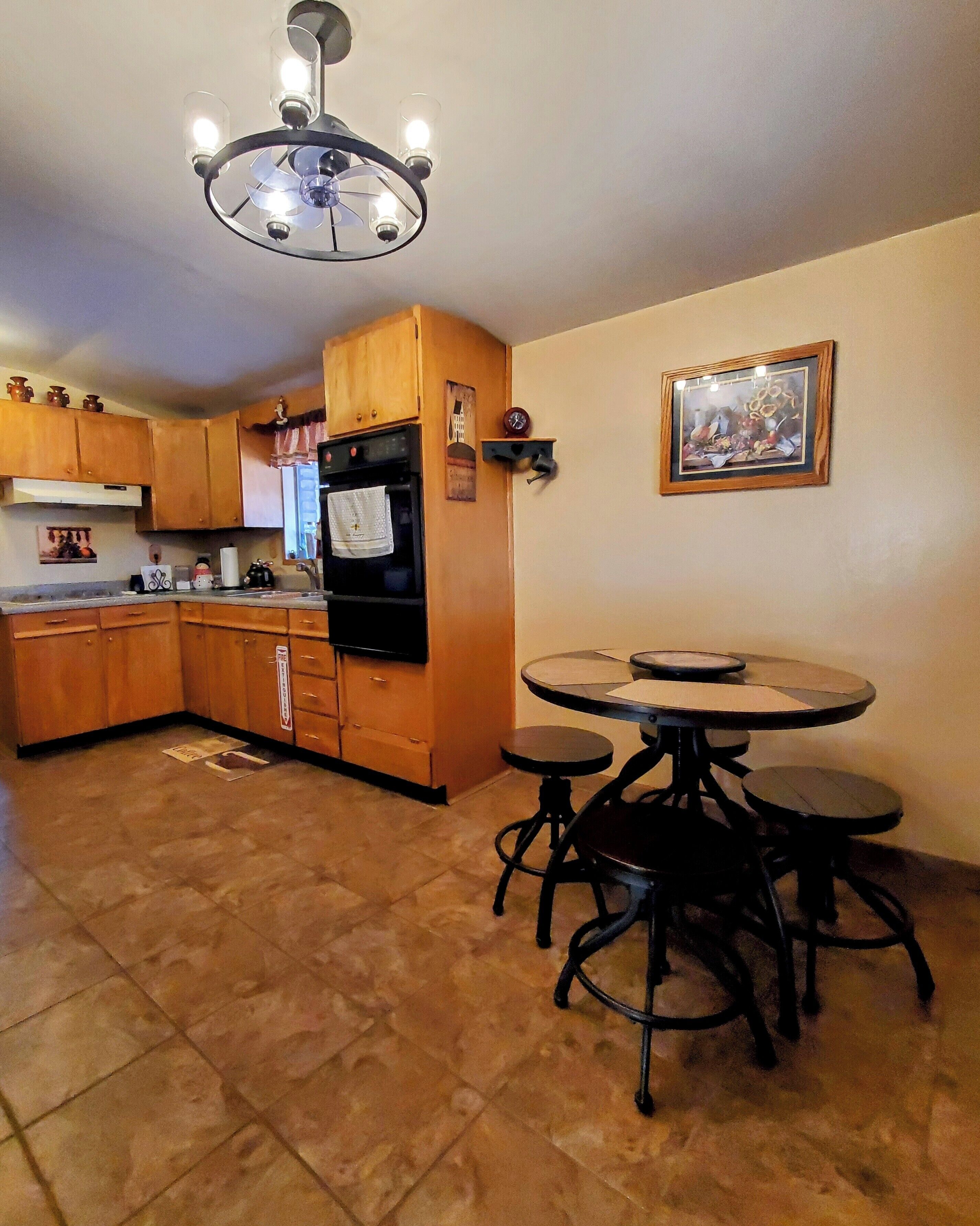 Una cocina con gabinetes de madera, un refrigerador negro, una estufa y una mesa de comedor con cuatro sillas.