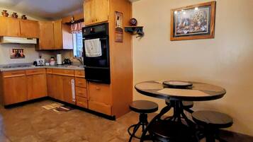Una cocina con gabinetes de madera, un refrigerador negro, una estufa y una mesa de comedor con cuatro sillas.
