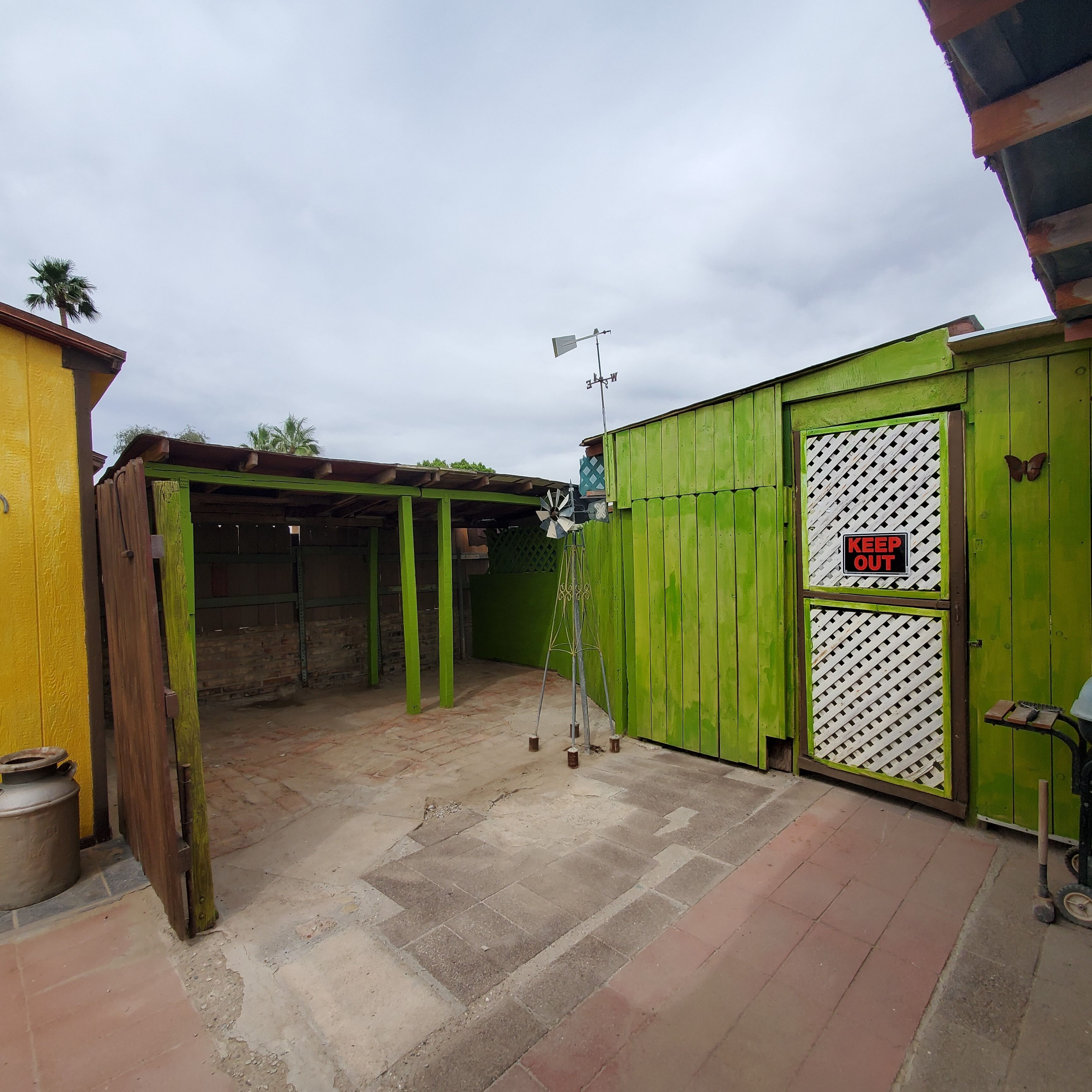 Una verja metálica verde con un cartel de 'KEEP OUT', un molino de viento y un piso de ladrillo.