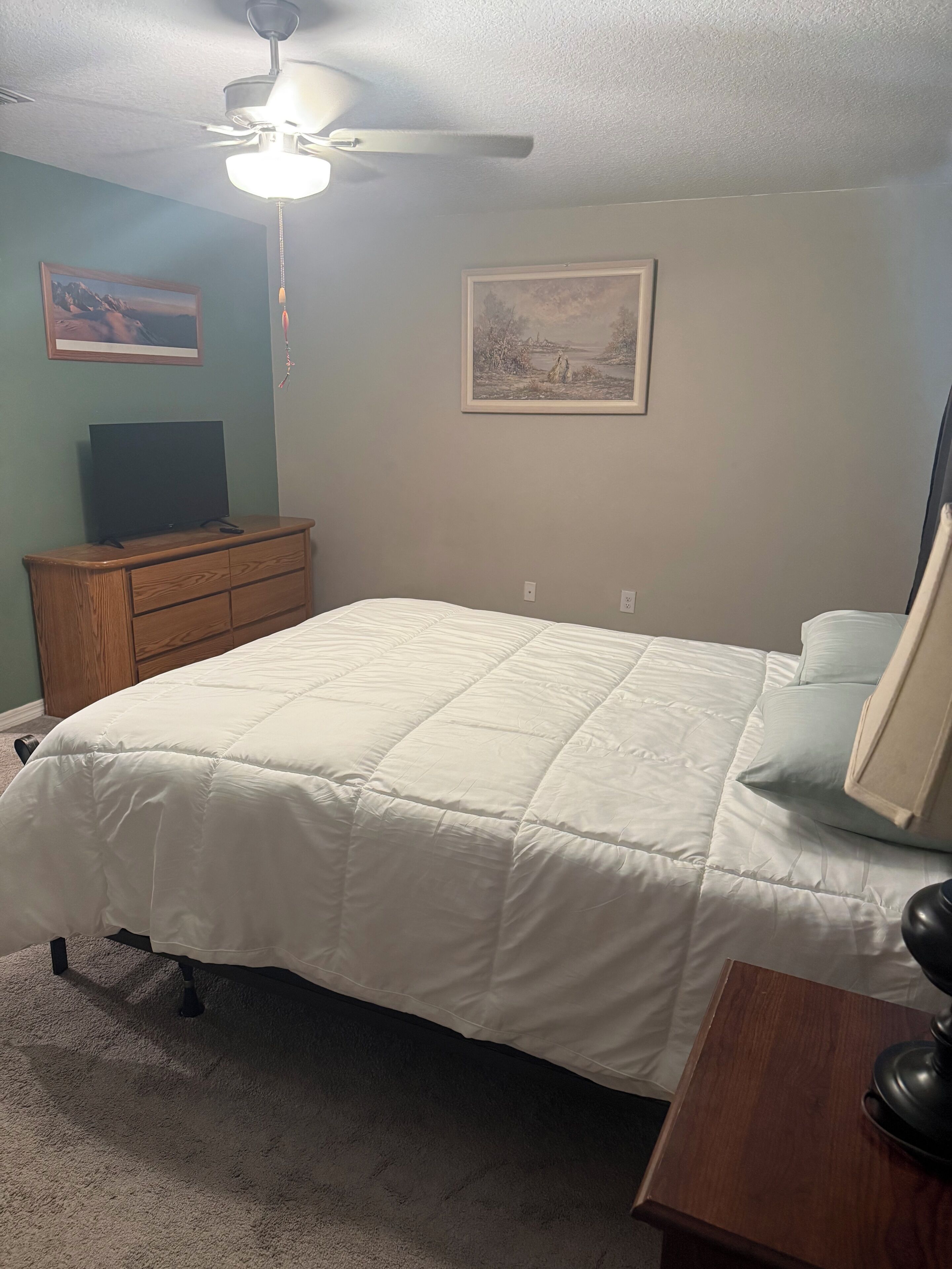 A bedroom with a bed, a dresser, a ceiling fan, and two framed pictures on the wall.