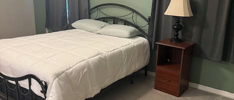 A bedroom with a bed, a nightstand, a lamp, a ceiling fan, and a painting on the wall.