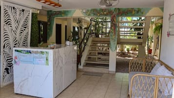 A reception area with a marble counter, a staircase leading to a covered outdoor area, and a wicker sofa.