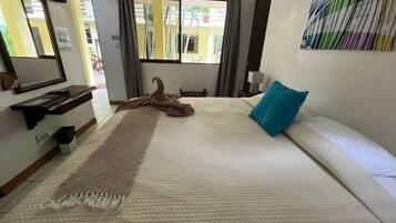 Habitación de hotel con cama, ventana grande, espejo, mesita de noche y una obra de arte colgada en la pared.