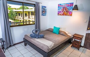 Un dormitorio con cama, ventana, un cuadro y una mesita de noche.
