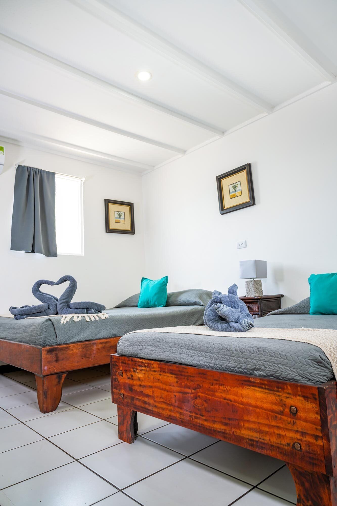 Ein Zimmer mit zwei Holzbetten, einem fenster mit Vorhängen und zwei gerahmten Bildern an der Wand.