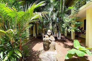 Un patio con una estatua, rodeado de exuberante follaje y plantas en macetas.