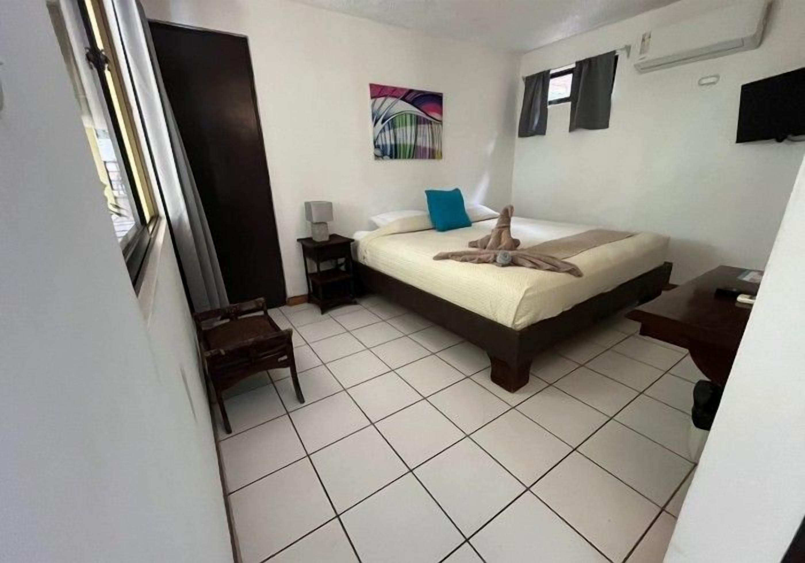 Un dormitorio con cama, una silla, una mesita de noche y una ventana.