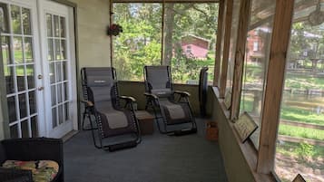 Une véranda abritée avec deux fauteuils inclinables, une petite table et une fenêtre donnant sur un bâtiment rouge et sur la verdure.