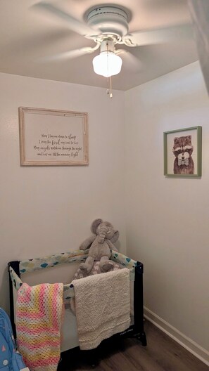 Ein Babybett mit Teddybär, einem gerahmten Motivationsspruch und einem gerahmten Bild von Tieren.