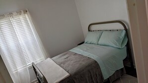 A single bed with a headboard, a bedside table, and a window with curtains. - Lakefront Retreat w/ Pool • Patio • Sleeps 7–8 • Fishing & Hunting Retreat (Huntsville)