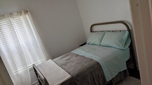 Ein Einzelbett mit Kopfstütze, ein Nachttisch und ein Fenster mit Vorhängen.
