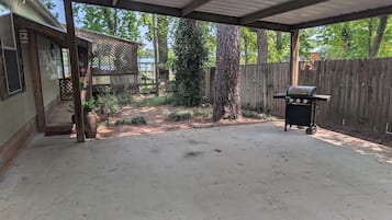 Une terrasse extérieure couverte, équipée d’un barbecue, entourée d’une clôture en bois et agrémentée d’un petit jardin.