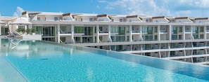 Un hôtel moderne doté d’une grande piscine, de nombreux balcons et offrant une vue sur un ciel d’un bleu éclatant.