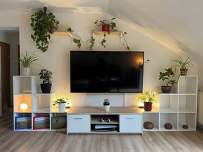 Una sala de estar con un televisor de pantalla plana montado en la pared, rodeada de estanterías y plantas en macetas.