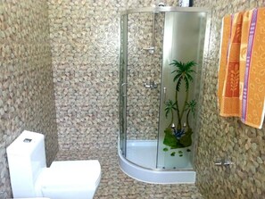 A bathroom with a glass-enclosed shower, a toilet, and a decorative wall with pebbles. - Namadi Nest Nuwara Eliya (Nuwara Eliya)