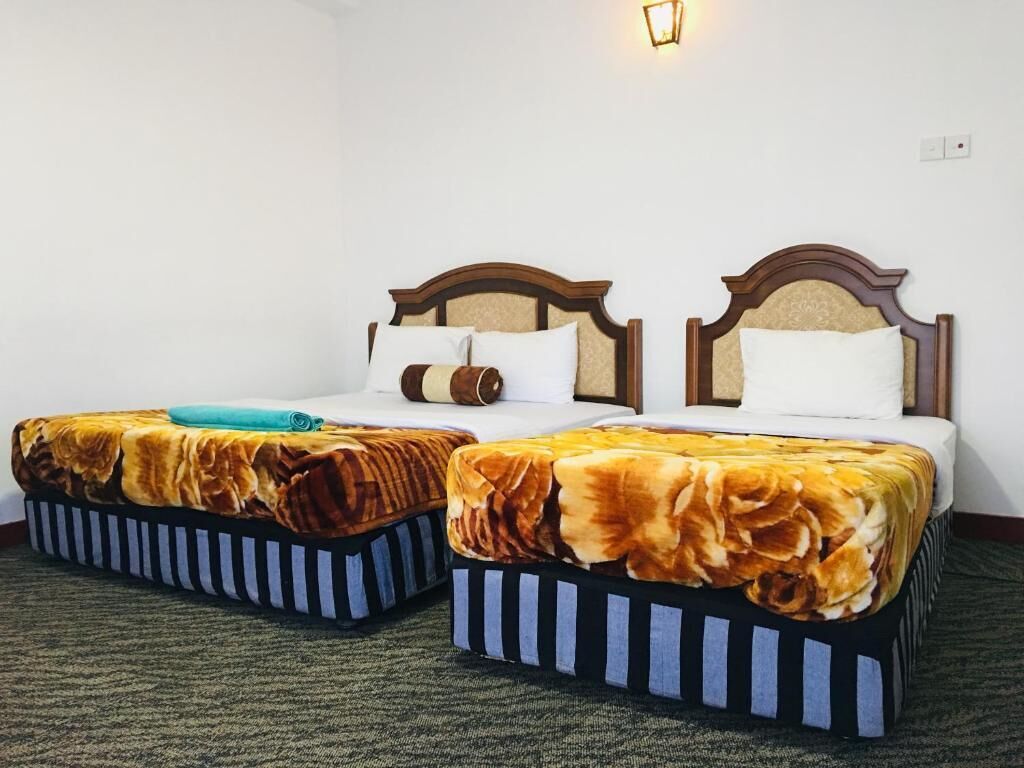 Two single beds with wooden headboards and striped footboards, a wall-mounted light fixture, and a carpeted floor.