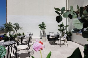 An outdoor patio area with multiple tables and chairs, surrounded by potted plants and a pink flower.