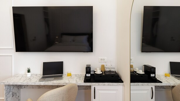 Una camera d'hotel con un letto, una scrivania con un portatile, una macchina del caffè e una TV fissata al muro.