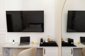 Habitació d'hotel amb un llit, una taula de treball amb un ordinador portàtil, una cafetera i un televisor penjat a la paret.