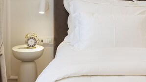 Una camera d'albergo con un letto, un comodino e un punto luce a parete.