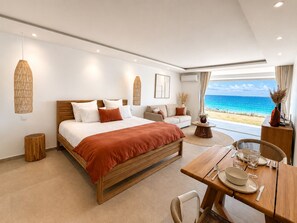 Un dormitorio moderno con una cama grande, un sofá, una mesa de comedor preparada para dos personas y vistas al océano.
